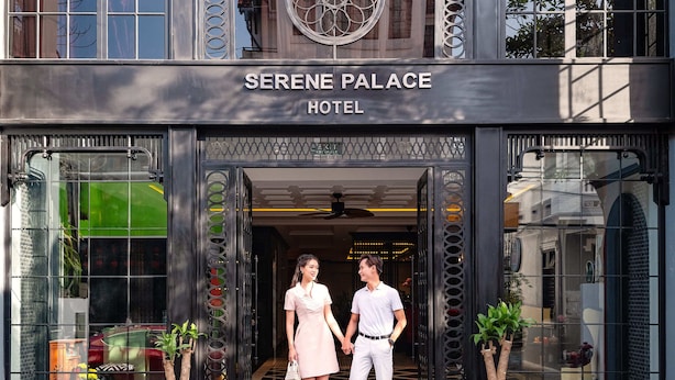 Entrada do Hotel Serene Palace com design moderno, apresentando uma grande janela em arco e uma placa sobre a entrada.