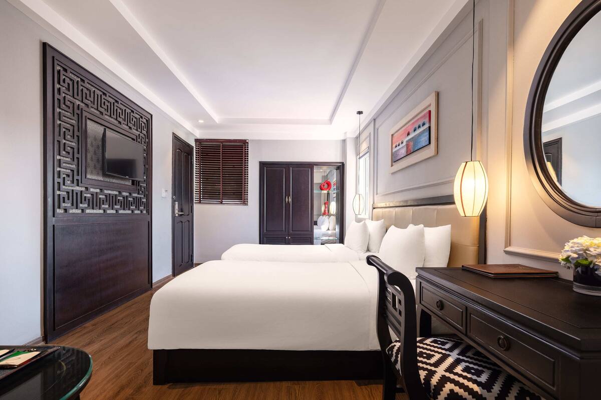 A hotel room with a large bed, a desk, a chair, a dresser, a mirror, and a window with blinds.