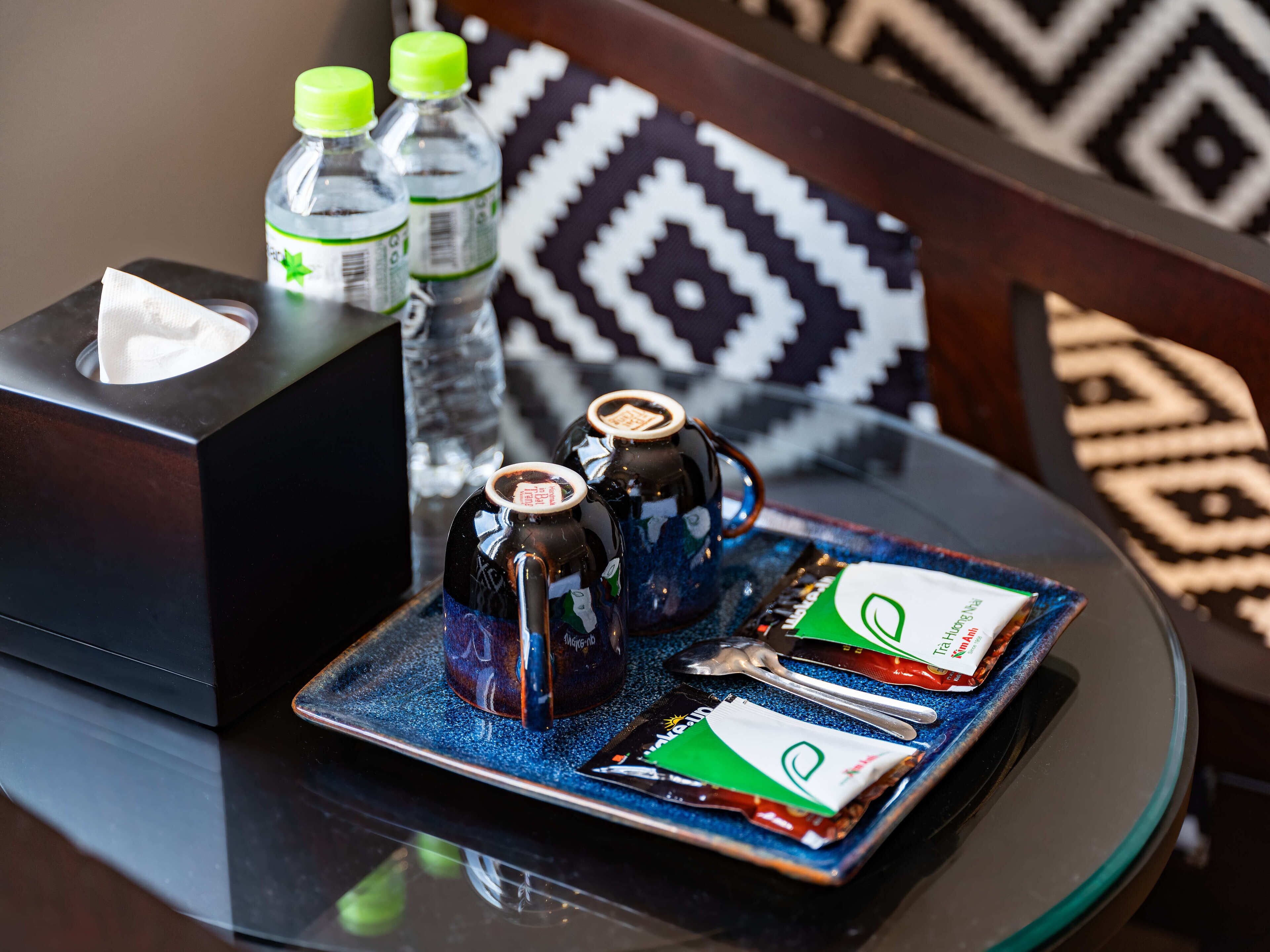 A tray with two teapots, a bottle of water, and a packet of snacks on a glass table.
