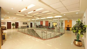 A spacious lobby with a central staircase, multiple seating areas, and a large potted plant. - Hotel Grand Mumtaz Towers (Srinagar)