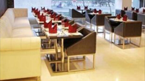 A modern hotel lobby with a row of tables and chairs, a sofa, and large windows offering a view of the cityscape. - Hotel Grand Mumtaz Towers (Srinagar)