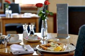 Une table de petit-déjeuner avec des toasts, des œufs et un vase de roses rouges.