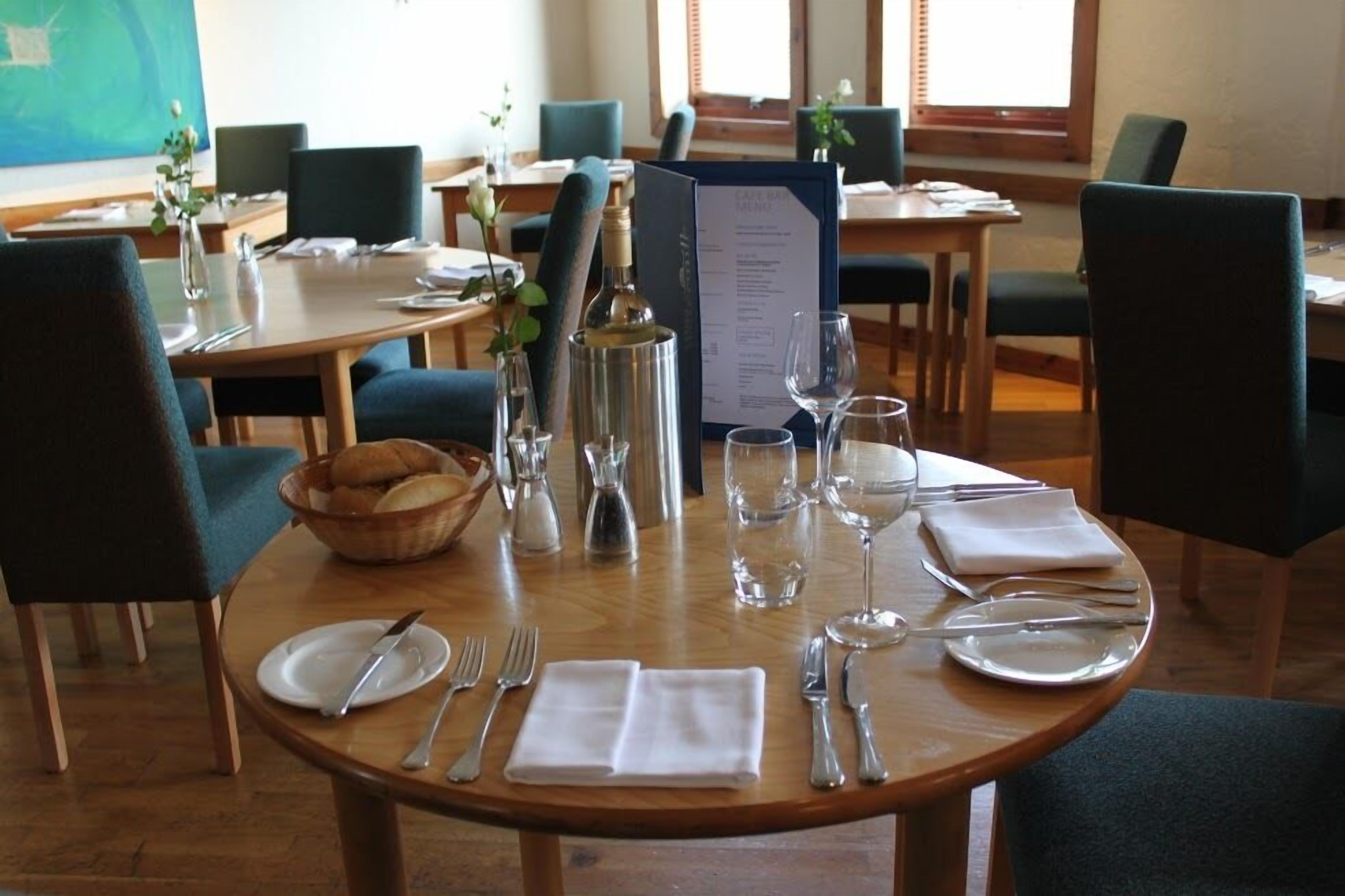 A dining area with round tables set for four, each with a menu, wine glass, and cutlery.