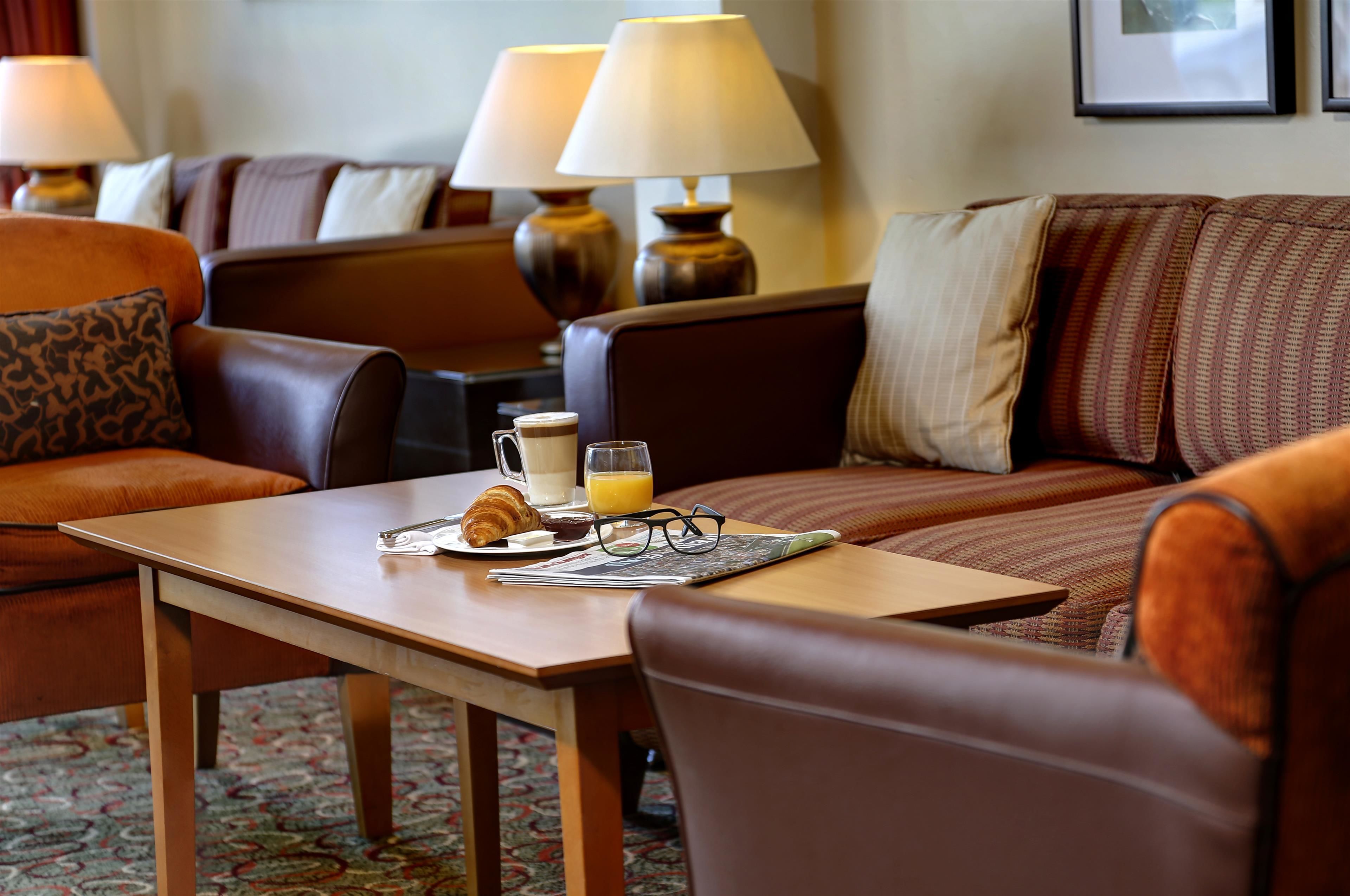 A hotel room with a dining table set with breakfast items, a sofa, and lamps.