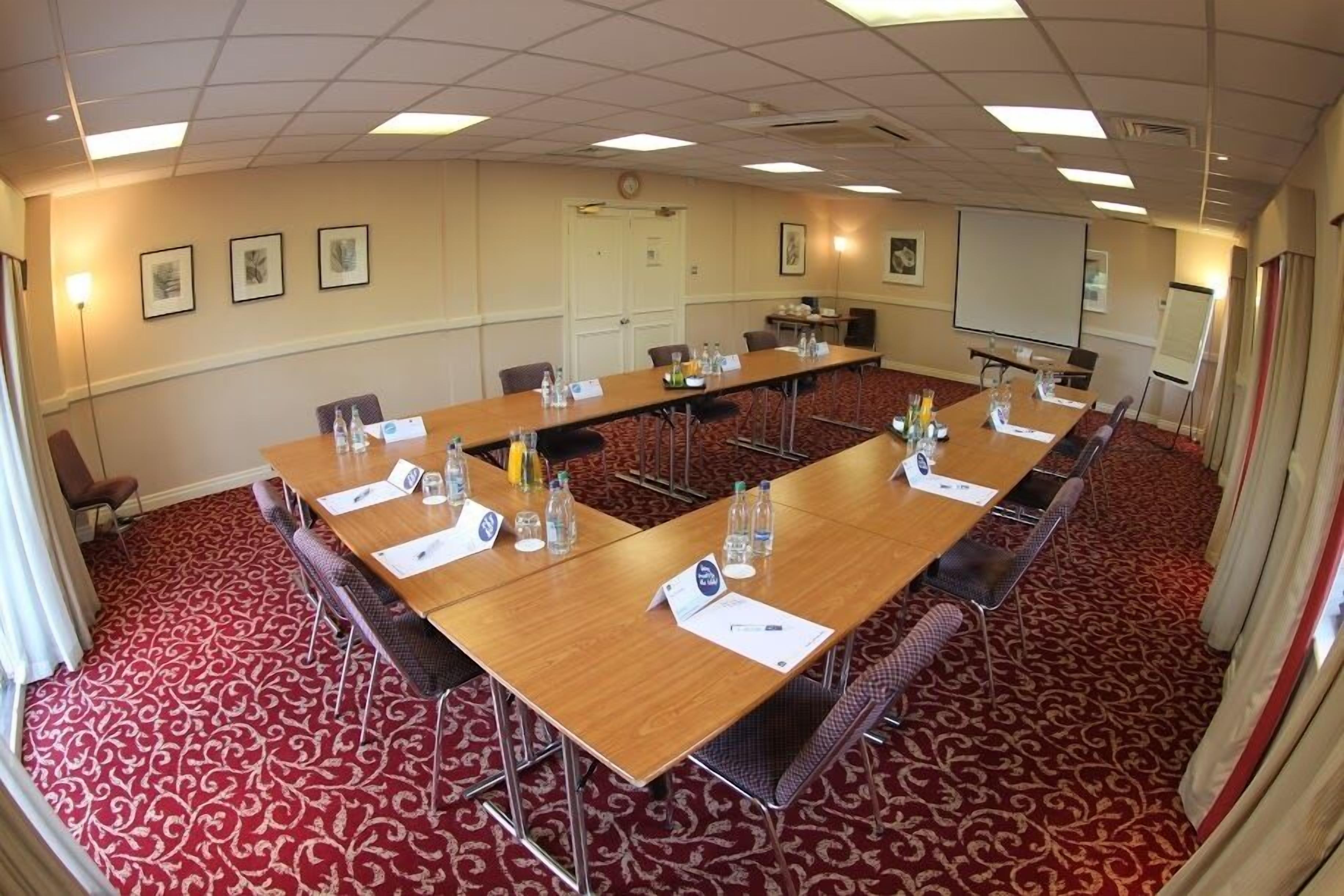 A conference room with a long table, chairs, nameplates, water bottles, and a projector screen.