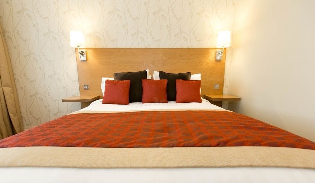 Una cama bien hecha con una colcha estampada, dos lámparas de noche y un cabecero de madera.