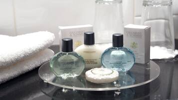 A bathroom counter with Gilchrist & Soames body lotion, shampoo, and body wash bottles, a white towel, and a glass jar.