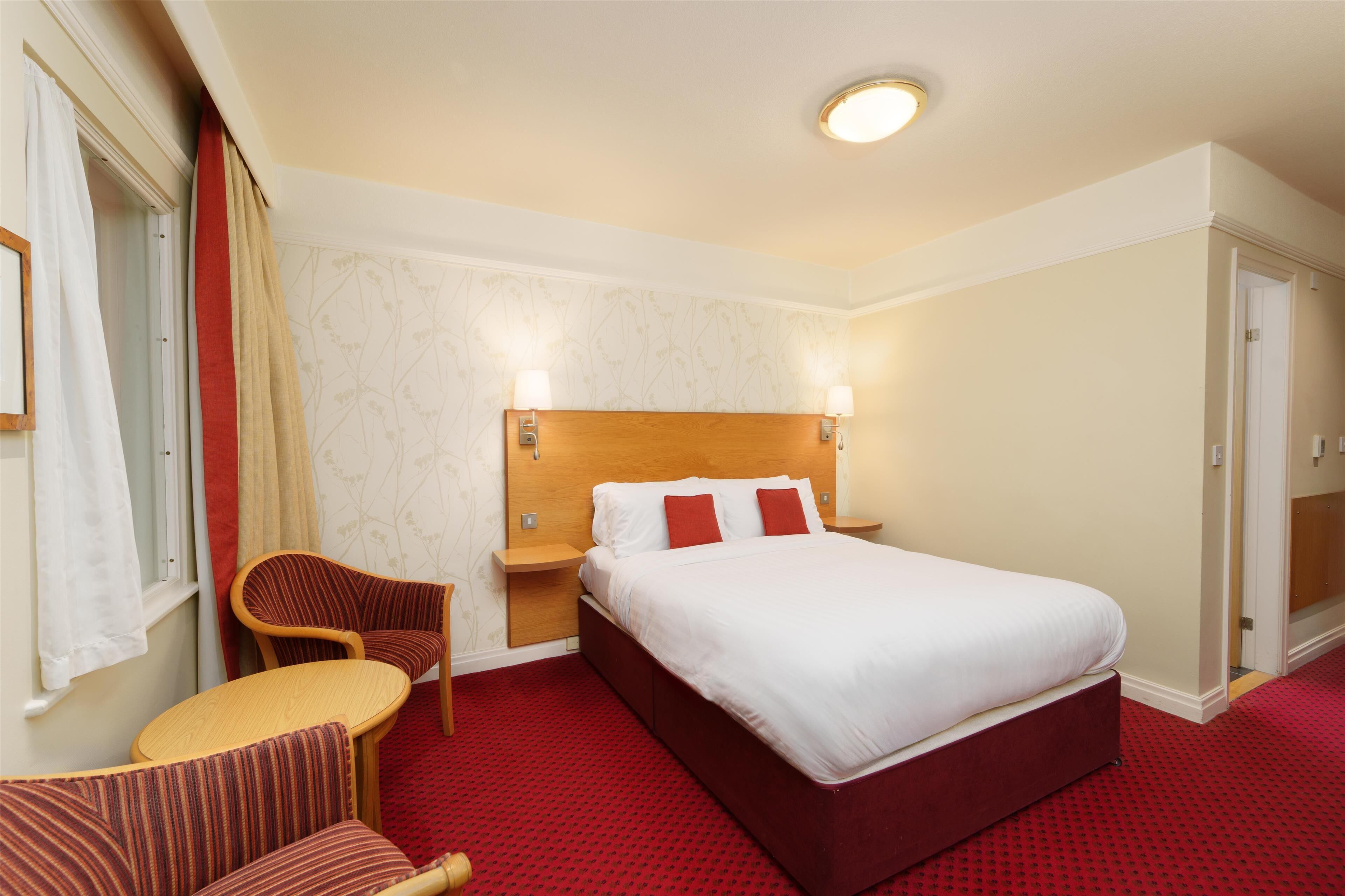Una habitación de hotel con una cama grande, dos mesitas de noche, una silla y una pequeña mesa.