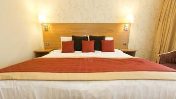 A hotel room with a wooden headboard, a large bed with a red and beige bedspread, and two bedside lamps.