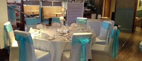 A round table set for a formal event with white chairs adorned with blue sashes.