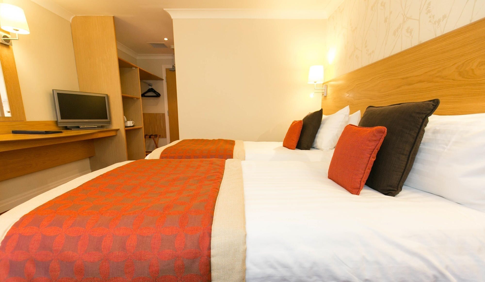 A hotel room with two beds, a TV, a desk, and a wardrobe.