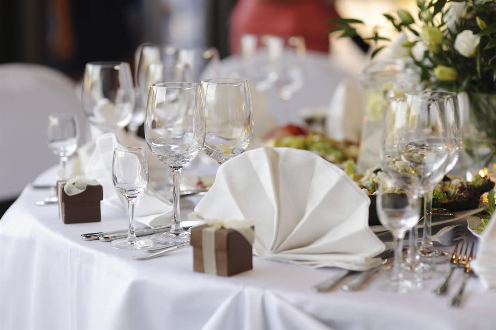 A table set for a formal event with multiple wine glasses, a fan, and a small gift box.