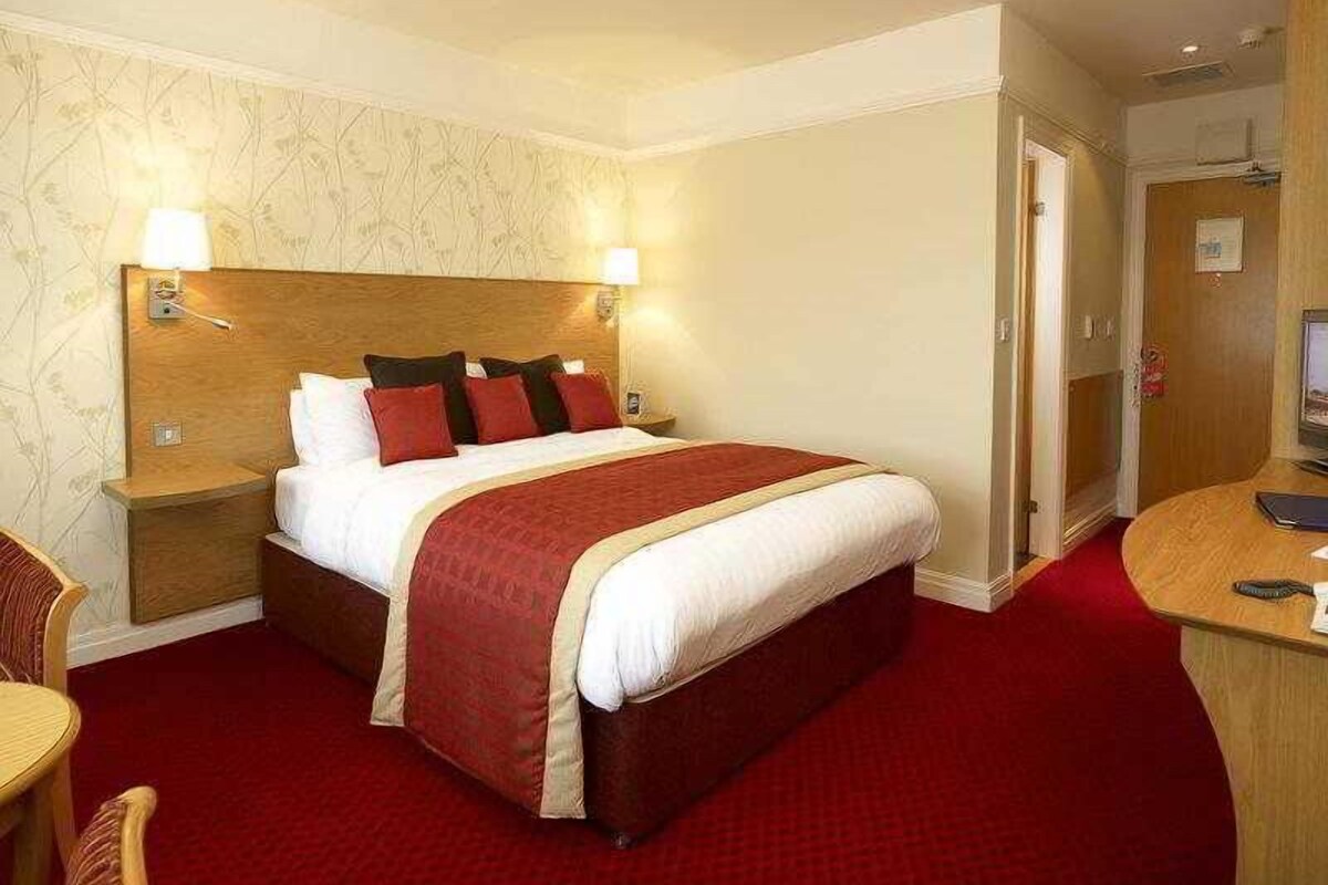 A hotel room with a large bed, bedside tables, a desk, and a chair.