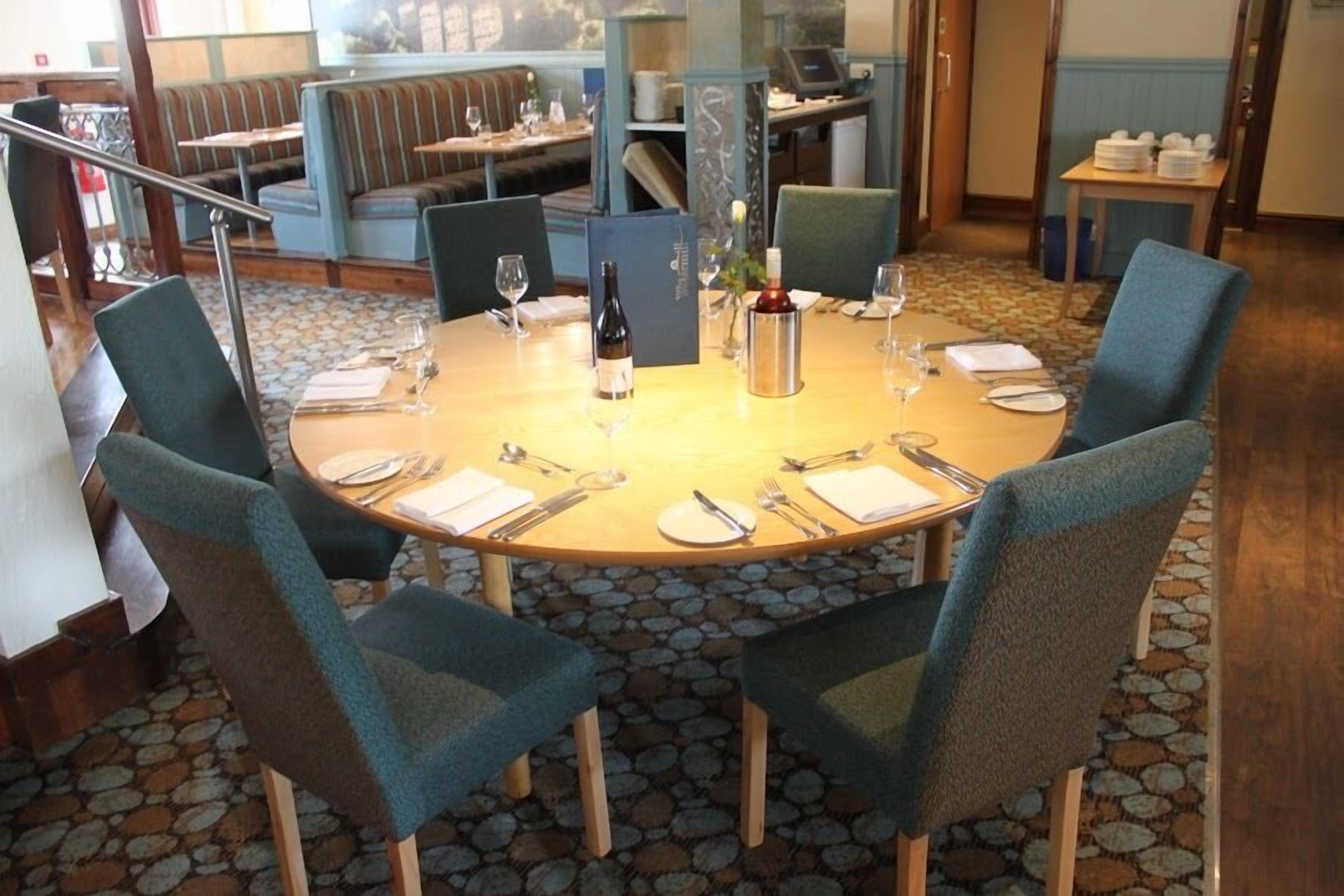 A round dining table with chairs, a bottle of wine, and a vase of flowers.