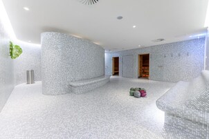Uma área de spa com piso de mosaico, espaço para sentar e porta de madeira que dá para outro cômodo.