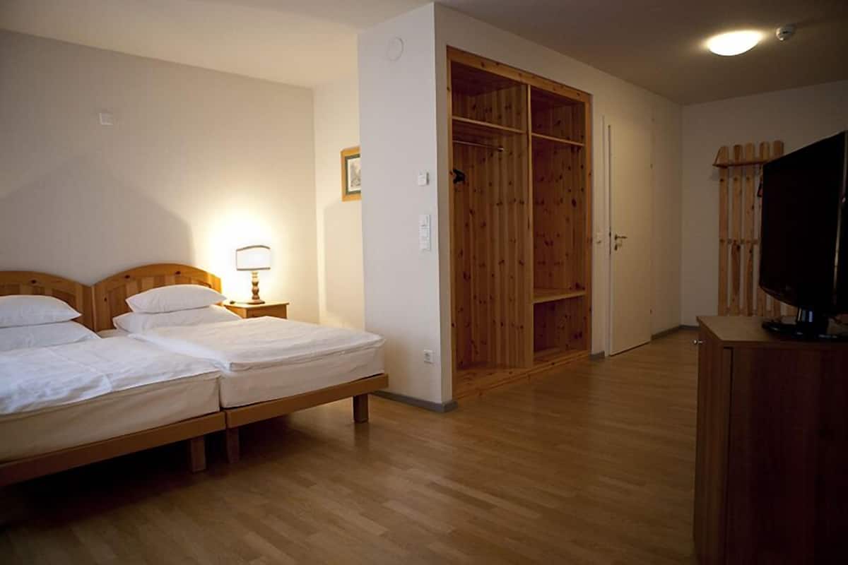 Un dormitorio con dos camas individuales, un armario de madera, un televisor y una mesita de noche con lámpara.