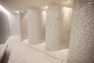 Casa de banho moderna com paredes e chão em mosaico, apresentando uma coluna central e um banco.