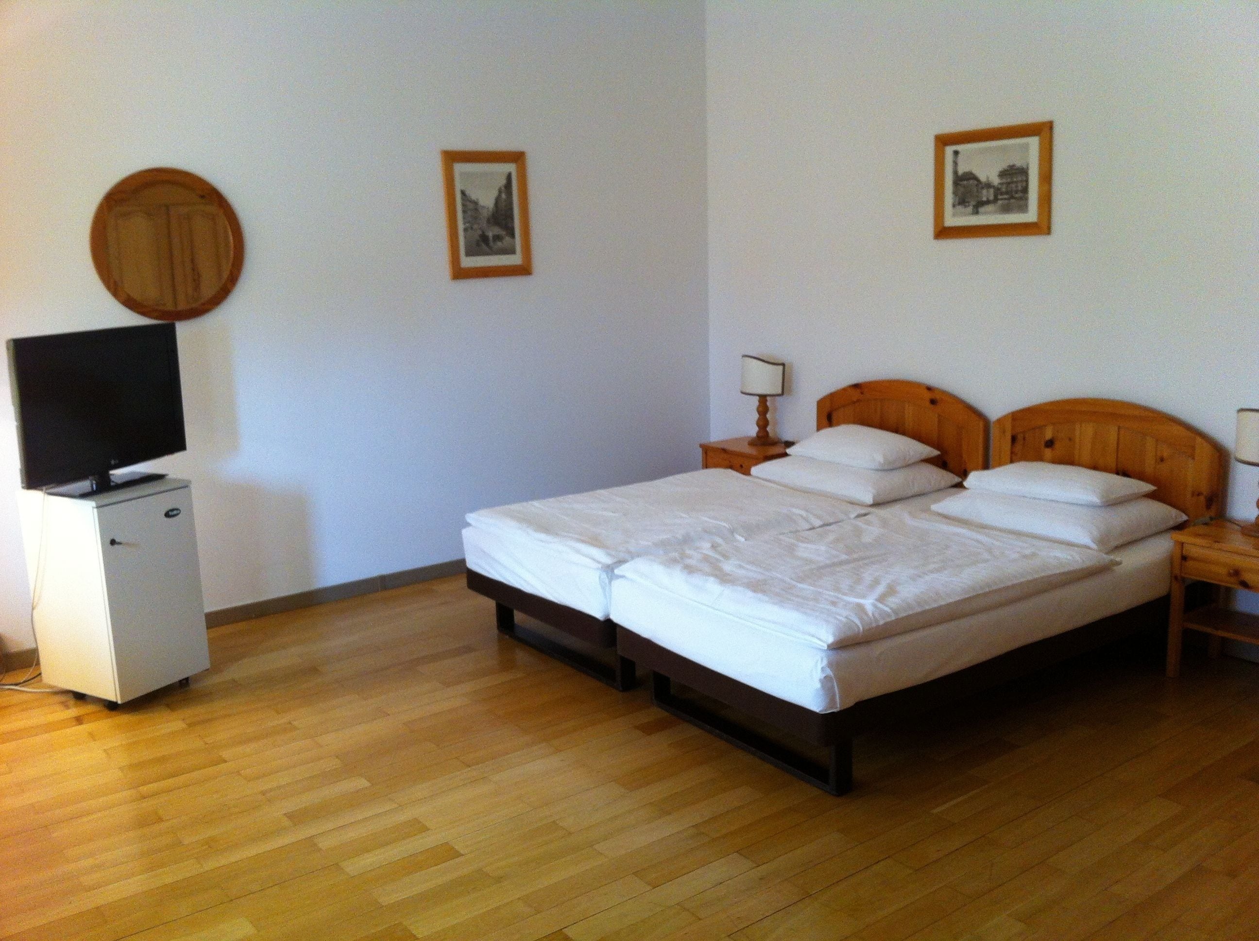 A bedroom with a bed, a TV on a cabinet, and two framed pictures on the wall.