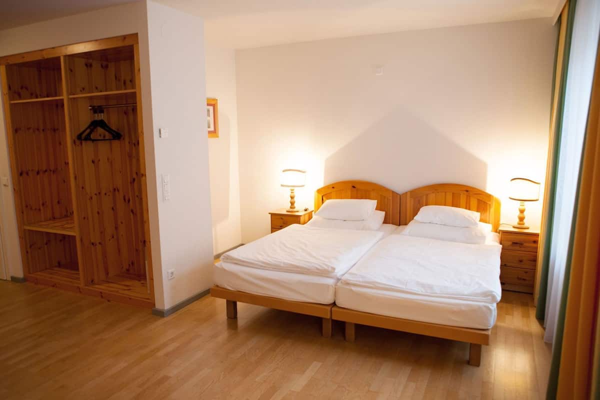 Cama doble con cabecera de madera, dos mesitas de noche con lámparas y un armario de madera con barra para colgar.