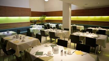 Un comedor con varias mesas redondas cubiertas con manteles blancos, sillas verdes y diferentes utensilios para comer.