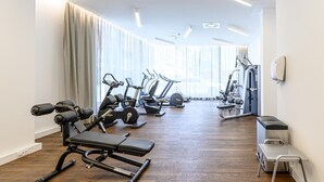 Un gimnasio moderno con diversos equipos de ejercicio, amplias ventanas y un interior luminoso y limpio.