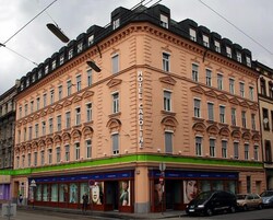 Un hotel a più piani con uno stile architettonico classico, caratterizzato da un ingresso in evidenza con tenda verde e numerose finestre.
