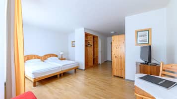 A hotel room with two beds, a wooden wardrobe, a television, and a desk with a laptop.