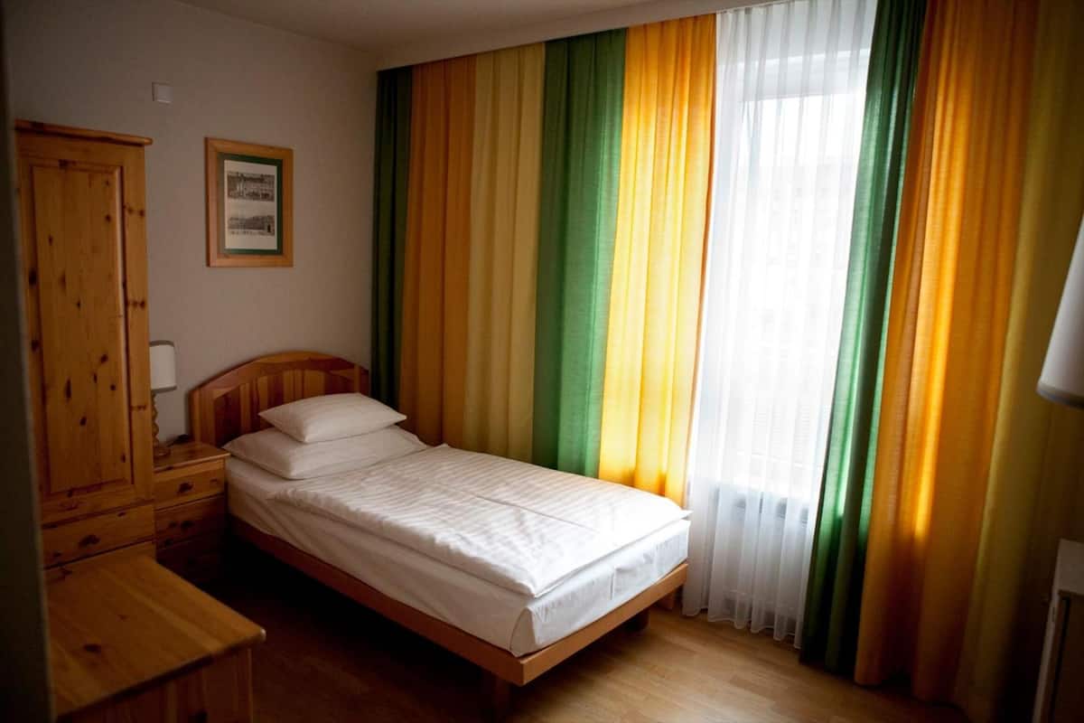 Una cama individual con cabecera de madera, una mesita de noche de madera, un armario de madera y un cuadro en la pared.