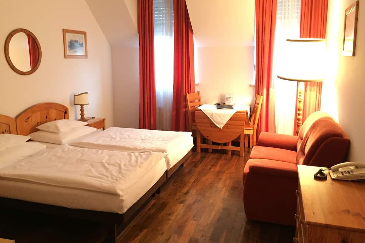 Habitación de hotel con dos camas, un escritorio, una silla, un sofá, un espejo y un cuadro en la pared.
