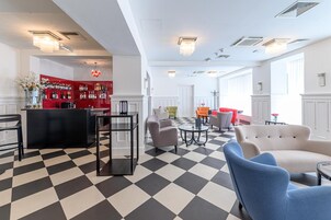 Um saguão de hotel com piso xadrez, área de bar com decoração vermelha e disposição de assentos.