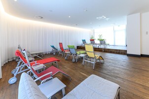 Um quarto com várias poltronas reclináveis e uma mesa, piso de madeira e janelas grandes com cortinas.