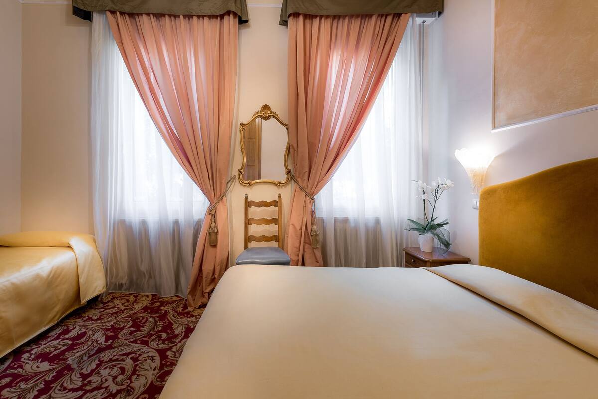 Una habitación de hotel con una cama grande, un cabecero de madera, una mesita de noche con lámpara y un espejo en la pared.
