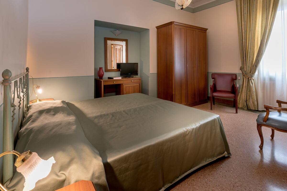 Una habitación de hotel con una cama, un televisor sobre un tocador de madera, un armario y dos sillas.