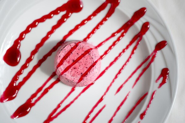 A dessert with a pink scoop and red sauce on a white plate.