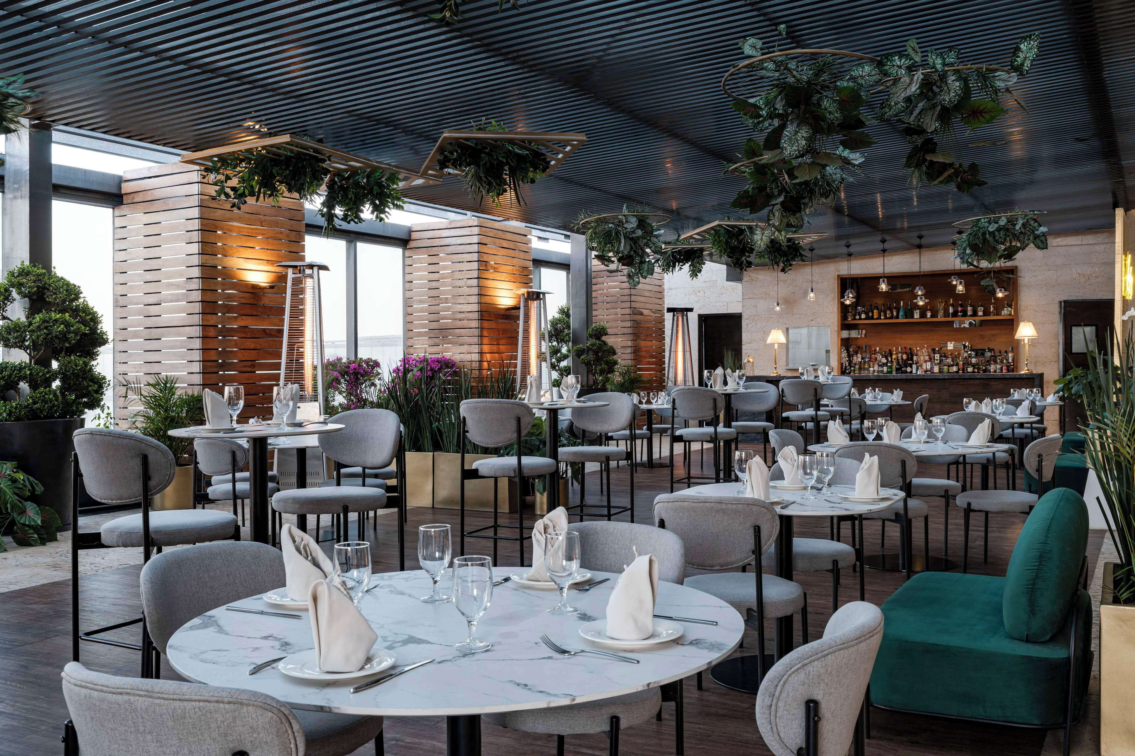 Un restaurant amb taules rodones, cadires grises i una zona de bar.