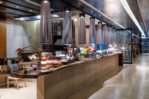 Zona de bufé con diversos alimentos, una barra de madera y lámparas colgantes.