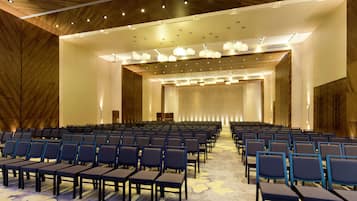 A conference room with rows of chairs, a stage, and a wooden ceiling with recessed lighting.