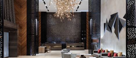 A modern lobby with a central seating area, a decorative chandelier, and a reception desk.