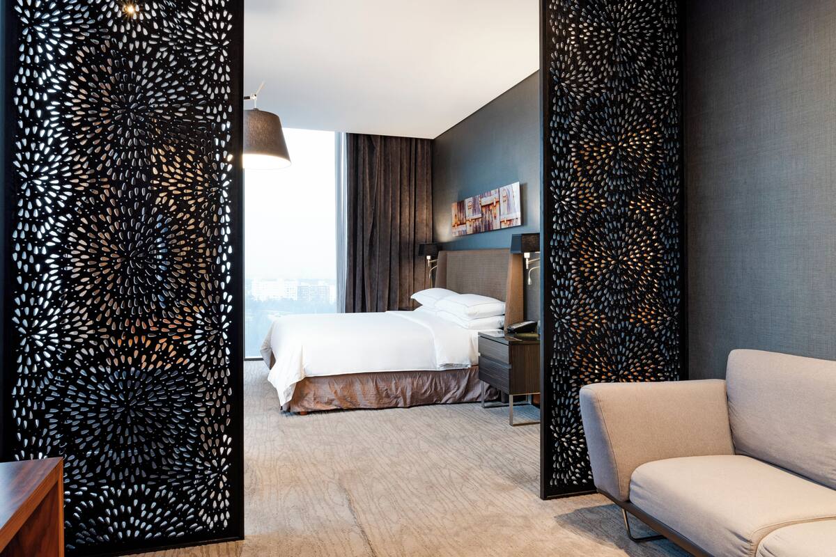 Una habitación de hotel moderna con cama, sofá, escritorio y un panel decorativo en la pared.
