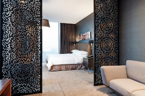 Una habitación de hotel moderna con cama, sofá, escritorio y un panel decorativo en la pared.