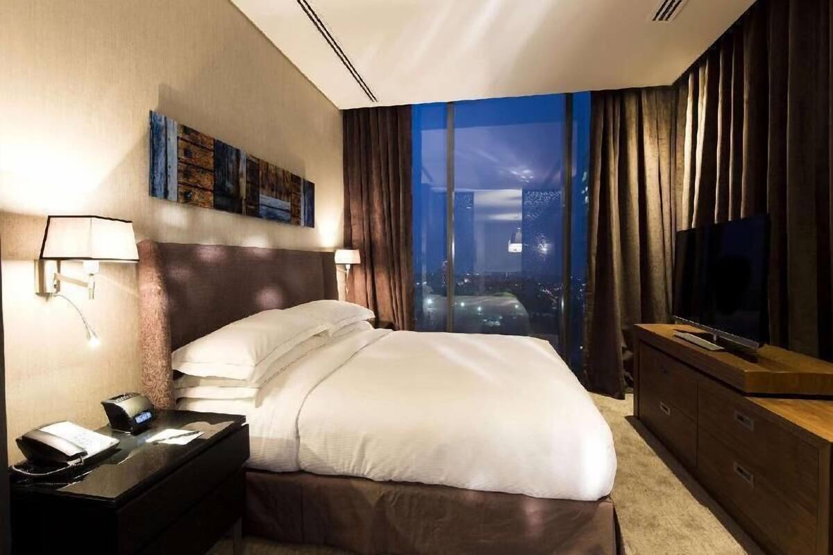Una habitación de hotel con una cama grande, televisión, mesita de noche con teléfono y vista a la ciudad de noche.