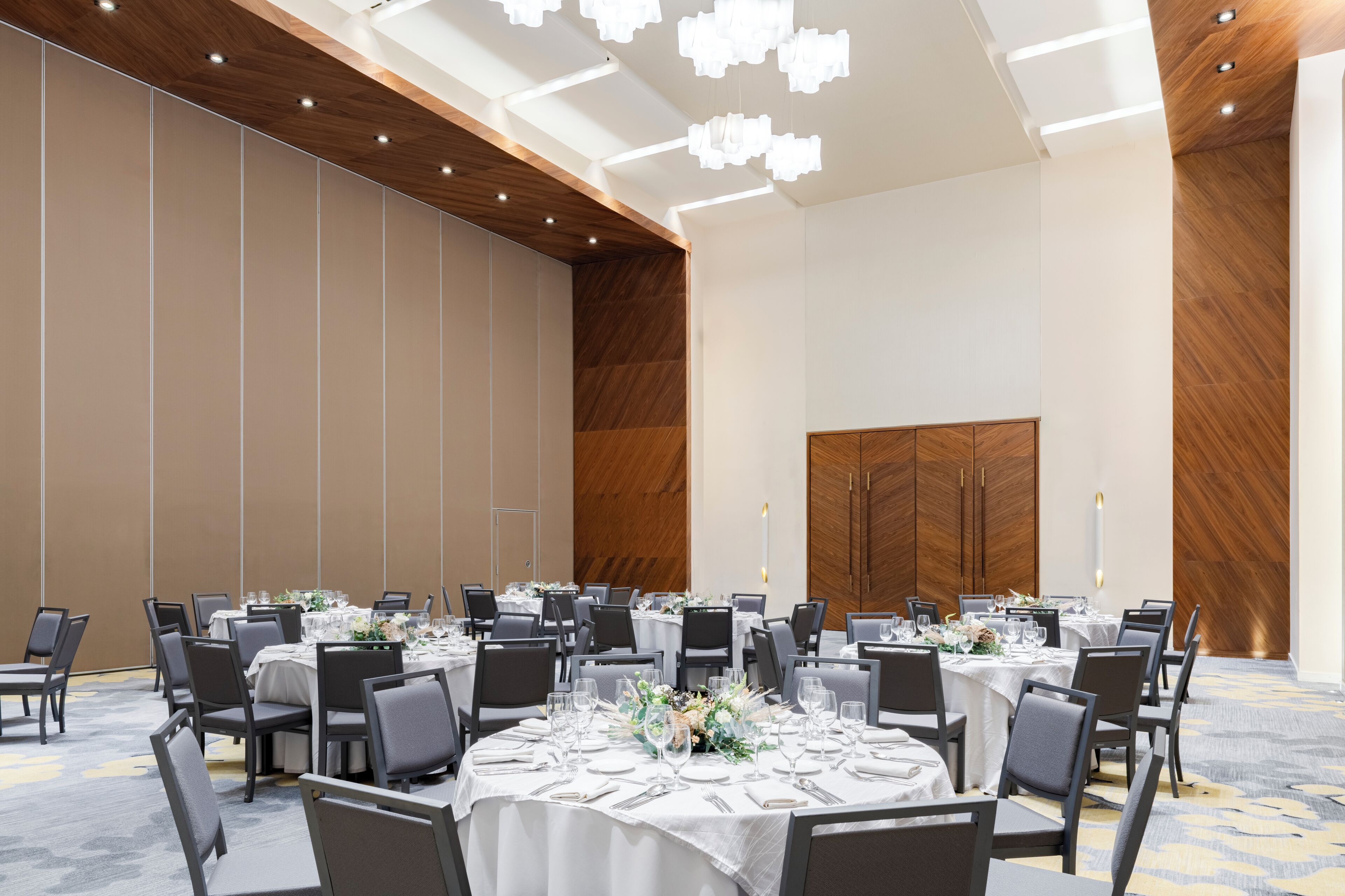 Une grande salle de conférence avec des tables rondes, des chaises grises et des nappes blanches.