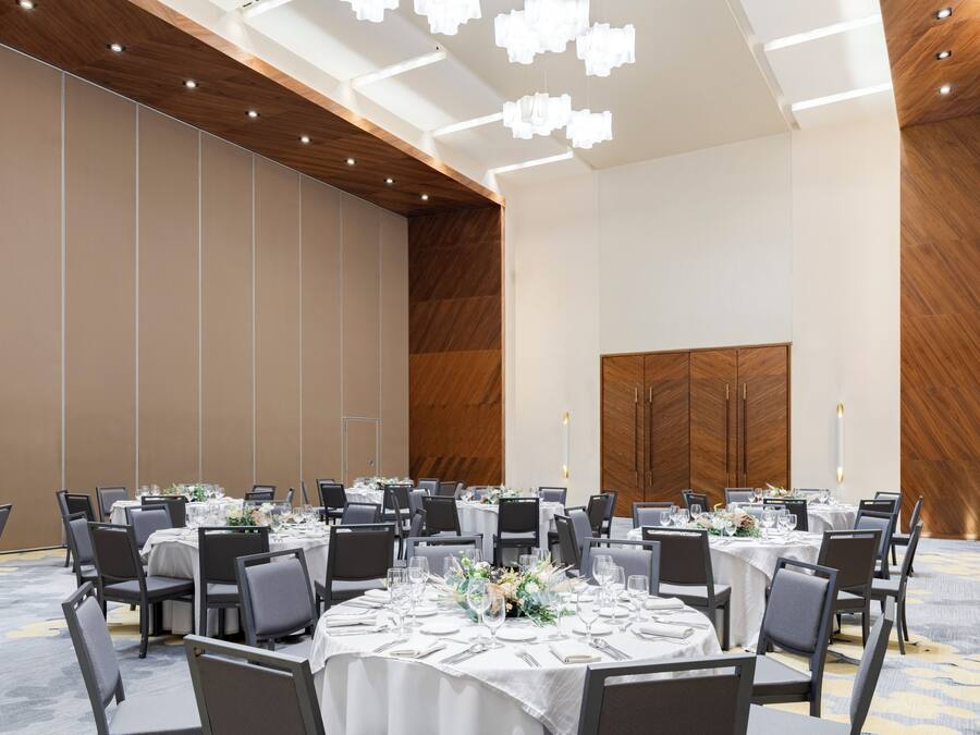 Une grande salle de conférence avec des tables rondes, des chaises grises et des nappes blanches.