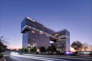 Un hotel moderno de varios pisos con un llamativo letrero 'Hilton', que presenta un diseño arquitectónico único con un gran voladizo.