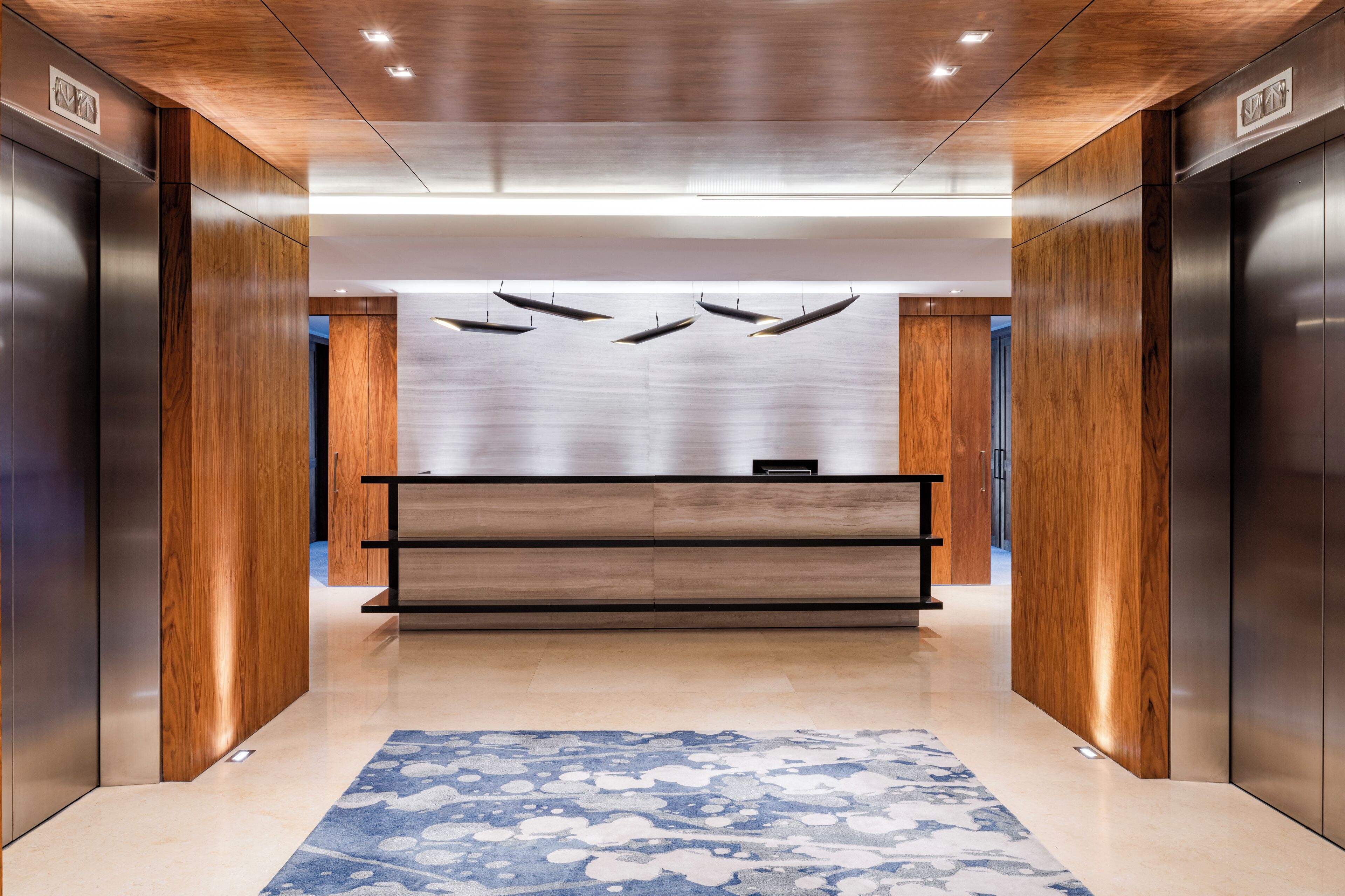 A modern elevator lobby with wooden paneling, a reception desk, and a patterned carpet.