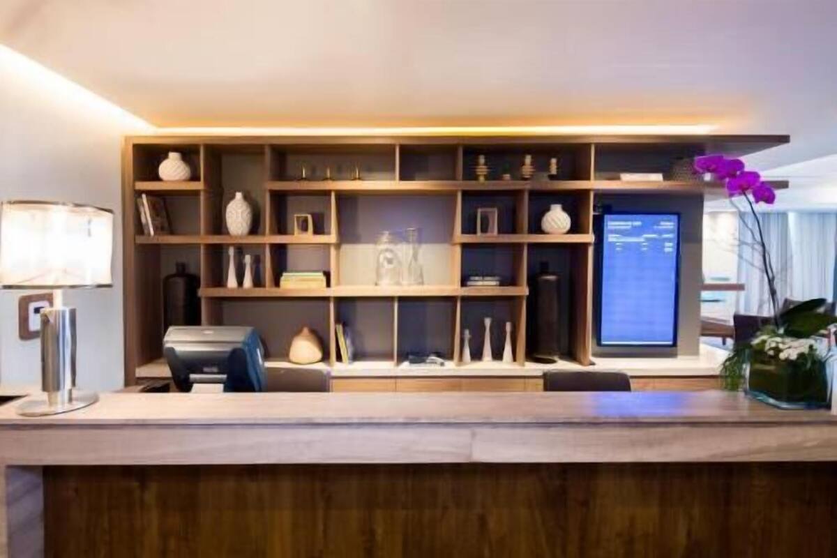 Un mostrador de recepción con un monitor de computadora, una lámpara y una estantería con diversos objetos decorativos.