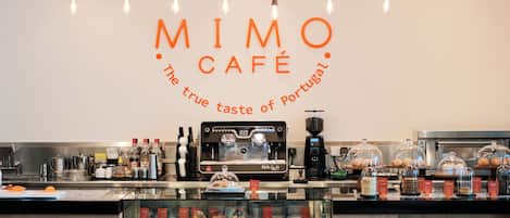 A café interior with a coffee machine, display case with pastries, and hanging light bulbs.