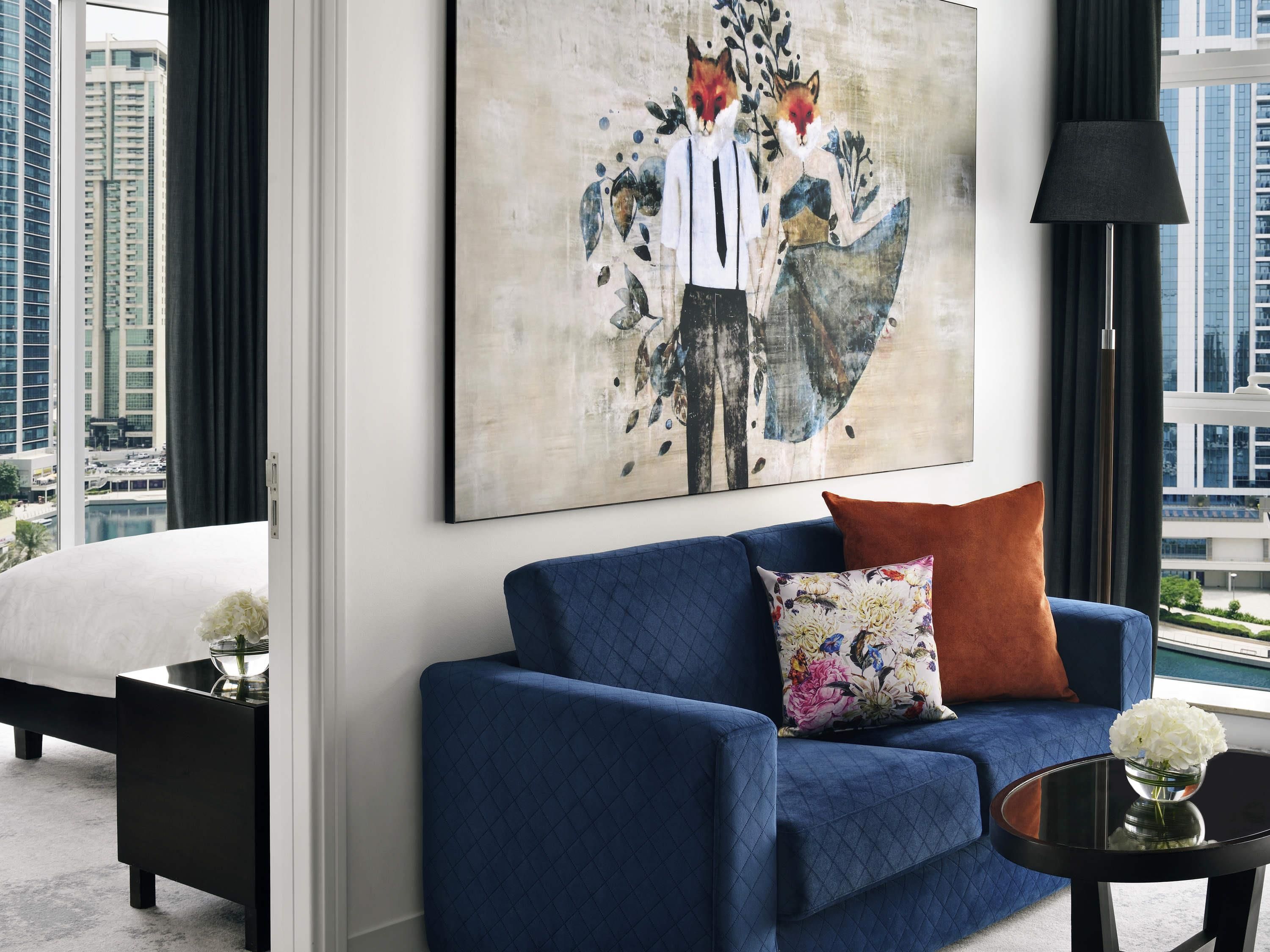 A modern living room with a blue sofa, a black side table, and a painting of foxes on the wall.