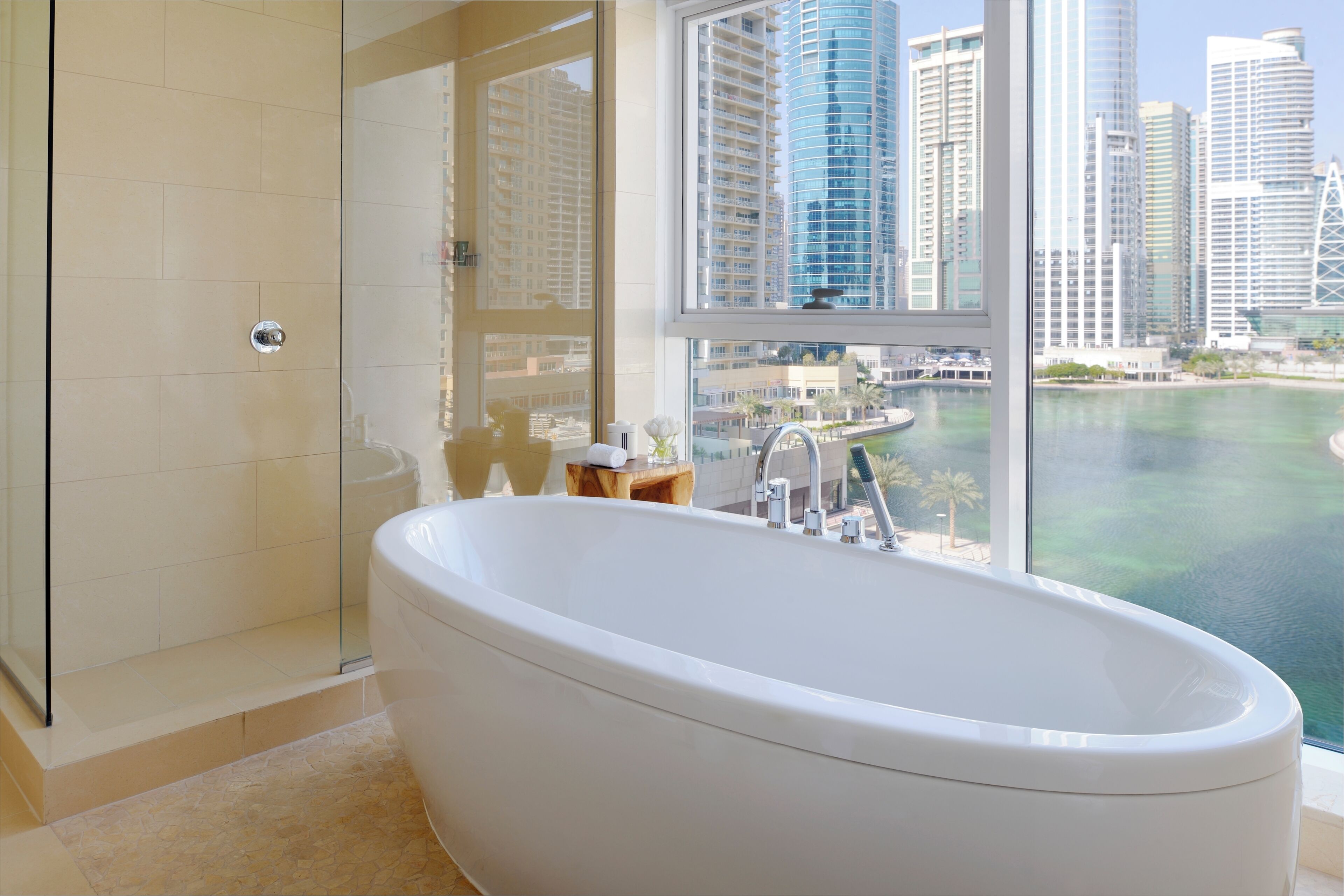 Une salle de bain moderne dotée d’une baignoire sur pieds, d’une douche à parois de verre et offrant une vue sur le paysage urbain et un plan d’eau.