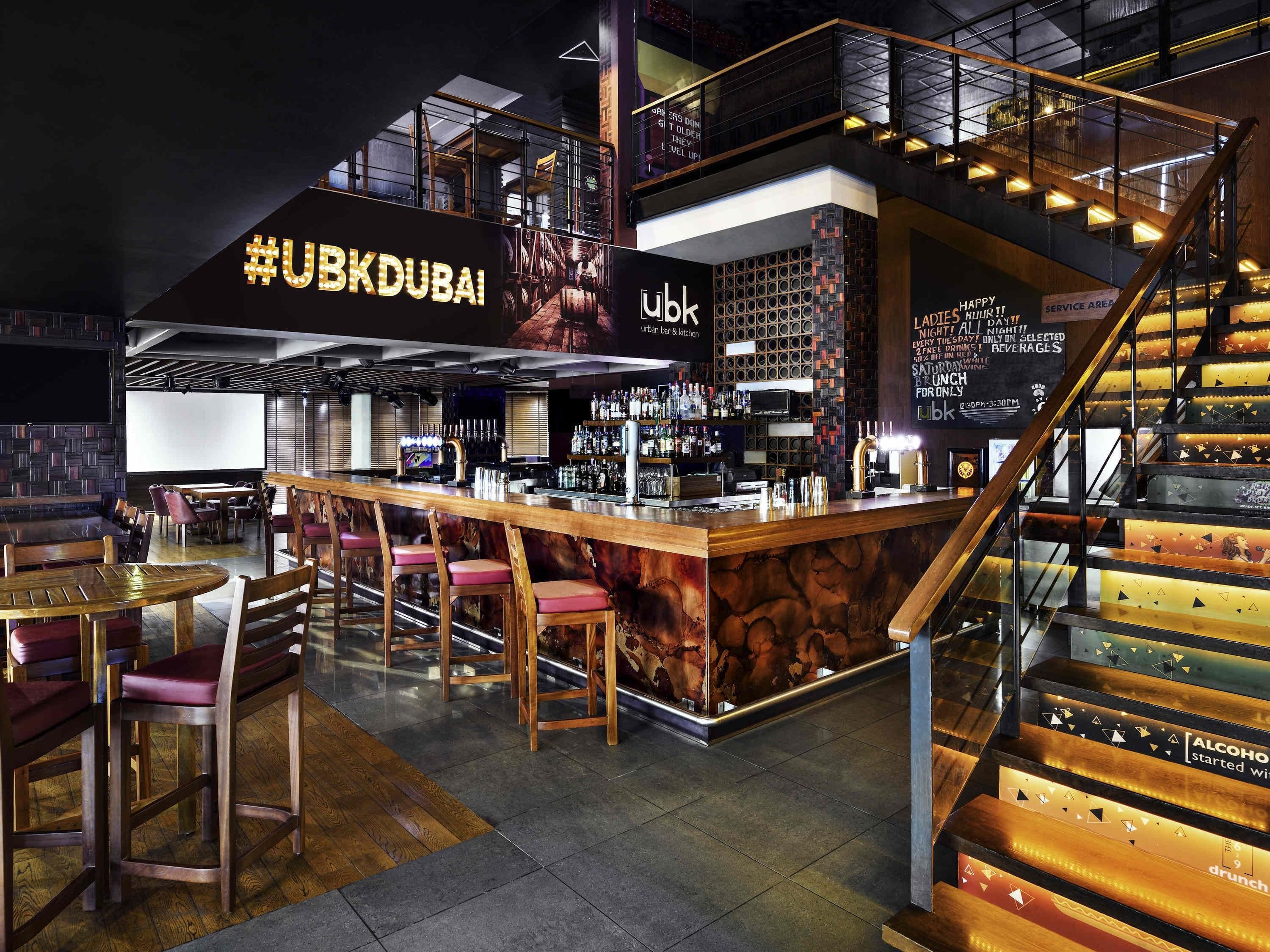 A modern bar area with a counter, stools, and a staircase.